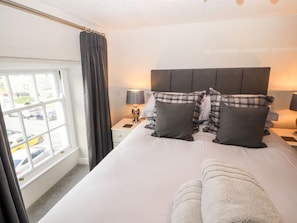 Una habitación de hotel con una cama grande, una ventana con cortinas, una mesita de noche con lámpara y vista a coches estacionados afuera.