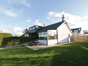 A modern house with a large glass window, a chimney, and a well-maintained lawn.