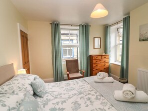 Ein Schlafzimmer mit Bett, Stuhl, Kommode und einem Fenster mit Vorhängen.