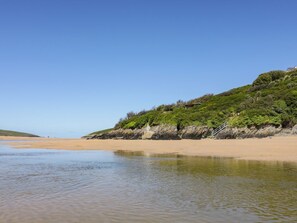 A beach with calm waters, a sandy shore, and a grassy hill with a structure on top. - Little Seacroft, Crantock (Newquay)