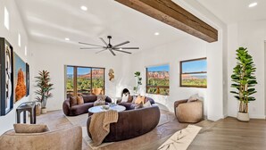 A spacious living room with a large window, a ceiling fan, and a fireplace. - Astra Sedona: NEW Luxury Home with Pool, Spa, Golf, Games & Stargazing Dome (Sedona)