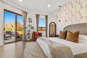 Une chambre avec un grand lit, une porte-fenêtre coulissante donnant sur un espace extérieur, une plante en pot et une vue sur une montagne.