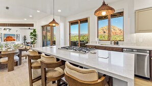 A modern kitchen with a large island, pendant lighting, and a view of a desert landscape. - Astra Sedona: NEW Luxury Home with Pool, Spa, Golf, Games & Stargazing Dome (Sedona)