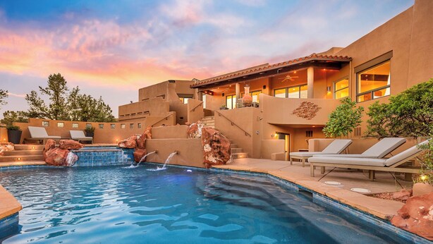 A swimming pool with a waterfall feature, lounge chairs, and a building with a terracotta facade. - Astra Sedona: NEW Luxury Home with Pool, Spa, Golf, Games & Stargazing Dome (Sedona)