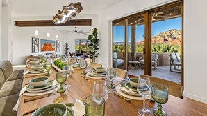 A dining area with a long table set for a meal, a ceiling fan, and a view of the outdoors. - Astra Sedona: NEW Luxury Home with Pool, Spa, Golf, Games & Stargazing Dome (Sedona)