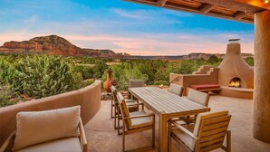 An outdoor patio with a table and chairs, a fire pit, and a view of a mountain range. - Astra Sedona: NEW Luxury Home with Pool, Spa, Golf, Games & Stargazing Dome (Sedona)