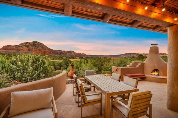 Une terrasse extérieure avec une table et des chaises, un foyer et une vue sur une chaîne de montagnes.