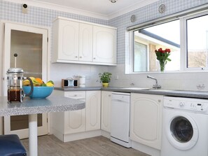Cocina compacta con armarios blancos, lavadora, lavaplatos y ventana con vistas.