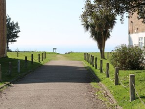 Un sendero pavimentado que lleva a un edificio con un muro de ladrillo y una entrada bordeada de árboles.