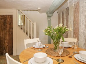 A dining table set for four with white plates, bowls, and wine glasses, a vase with flowers, and a woven placemat. - The Hideaway, Ottery St Mary (Ottery St. Mary)