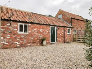A brick building with a tiled roof, a gravel driveway, and a wooden fence.