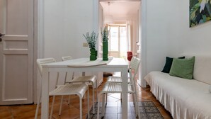 Un tavolo da pranzo bianco con sedie, un vaso verde e un divano bianco con un tappeto decorato.