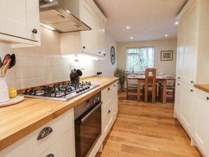 A kitchen with a gas stove, wooden countertop, white cabinets, and a dining area with a table and chairs. - Spindlewood Cottage, Hawkhurst (Cranbrook)