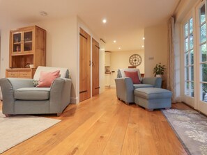 A living room with two sofas, a wooden cabinet, and a dining area with a clock. - Spindlewood Cottage, Hawkhurst (Cranbrook)