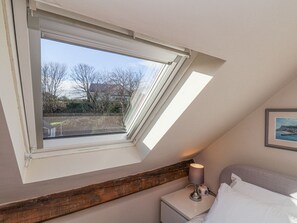 Ein Schlafzimmer mit Dachfenster, einem Nachttisch mit Lampe, einem Bett und einem gerahmten Bild an der Wand.