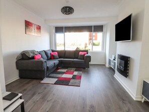 A living room with a sectional sofa, a flat-screen TV, and a fireplace. - Beach Side Bungalow, Lytham St. Annes (Lytham St. Annes)
