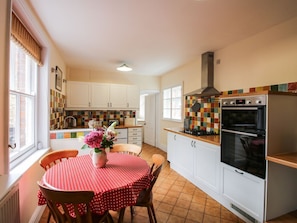 A kitchen with white cabinets, a tiled backsplash, a stove, and a dining area with a red tablecloth.