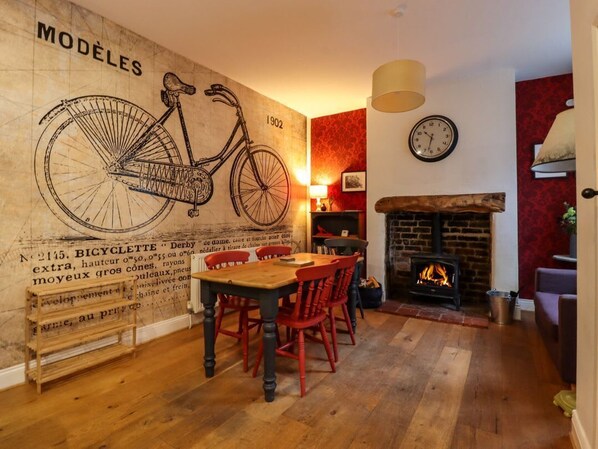 A dining area with a wooden table and chairs, a fireplace, and a wall with a bicycle illustration. - Castlewood Cottage, Skipton (Skipton)