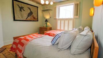 A bedroom with two beds, a window with shutters, a ceiling light fixture, and a wall-mounted lamp.
