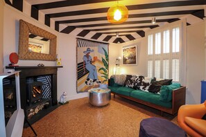 Ein Wohnzimmer mit Kamin, einem grünen Sofa, einem runden Hocker und einem Bild an der Wand.
