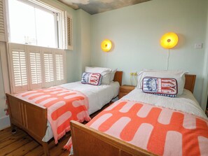 Een slaapkamer met twee eenpersoonsbedden, een houten vloer, een raam met luiken en een nachtkastje met een lamp.