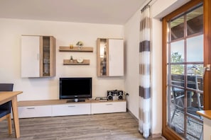 Ein modernes Wohnzimmer mit Flachbildfernseher, integrierten Regalen und einer Schiebeglastür zum Außenbereich.