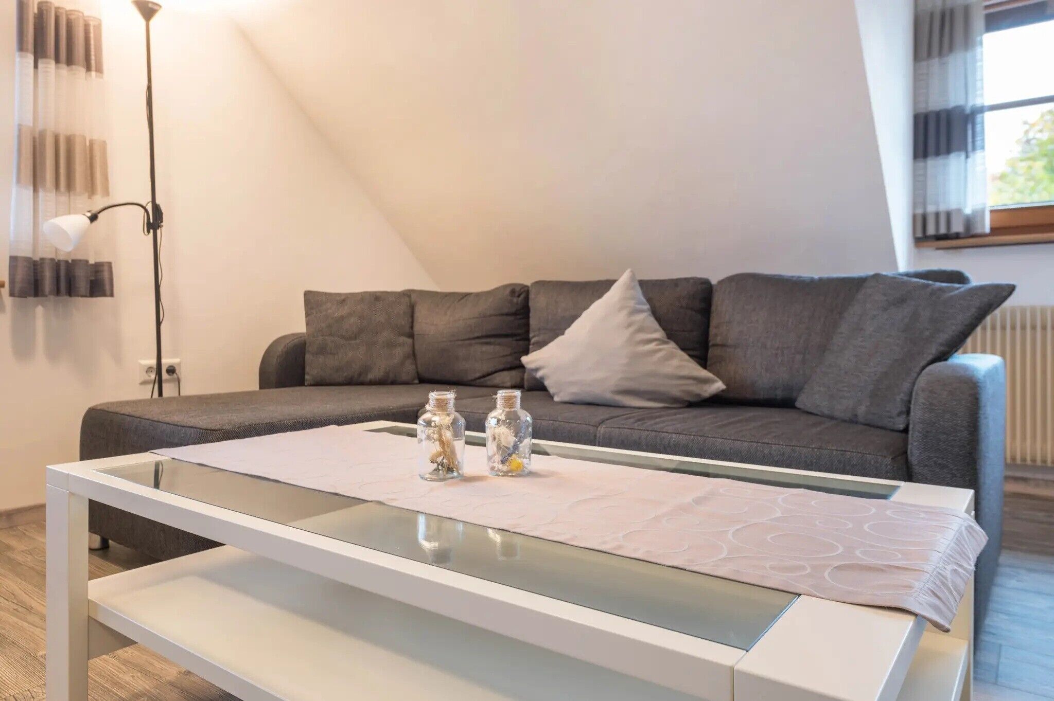 Un salon moderne avec un canapé gris, une table basse en verre et un lampadaire.