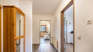Un couloir avec un cadre de porte en bois, un radiateur et une vue sur une pièce où se trouvent un lit et une fenêtre.