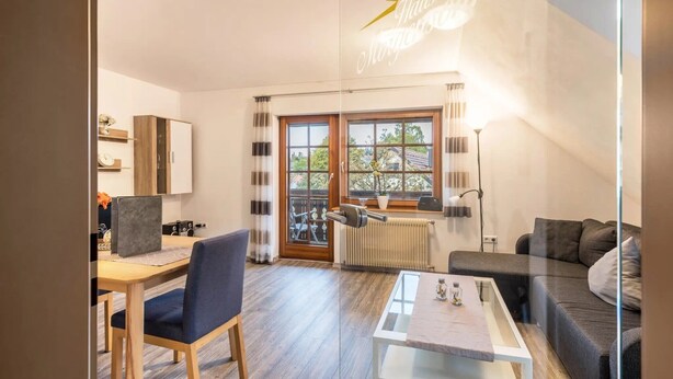 Un salon moderne comprenant un canapé, une table à manger avec des chaises, une cloison en verre, un radiateur et une fenêtre donnant sur l’extérieur.