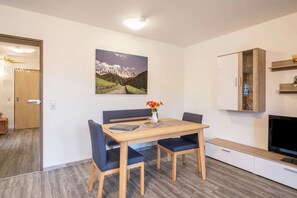 Ein modernes Zimmer mit Esstisch, Stühlen, einem Fernseher und einem Gemälde einer Berglandschaft.