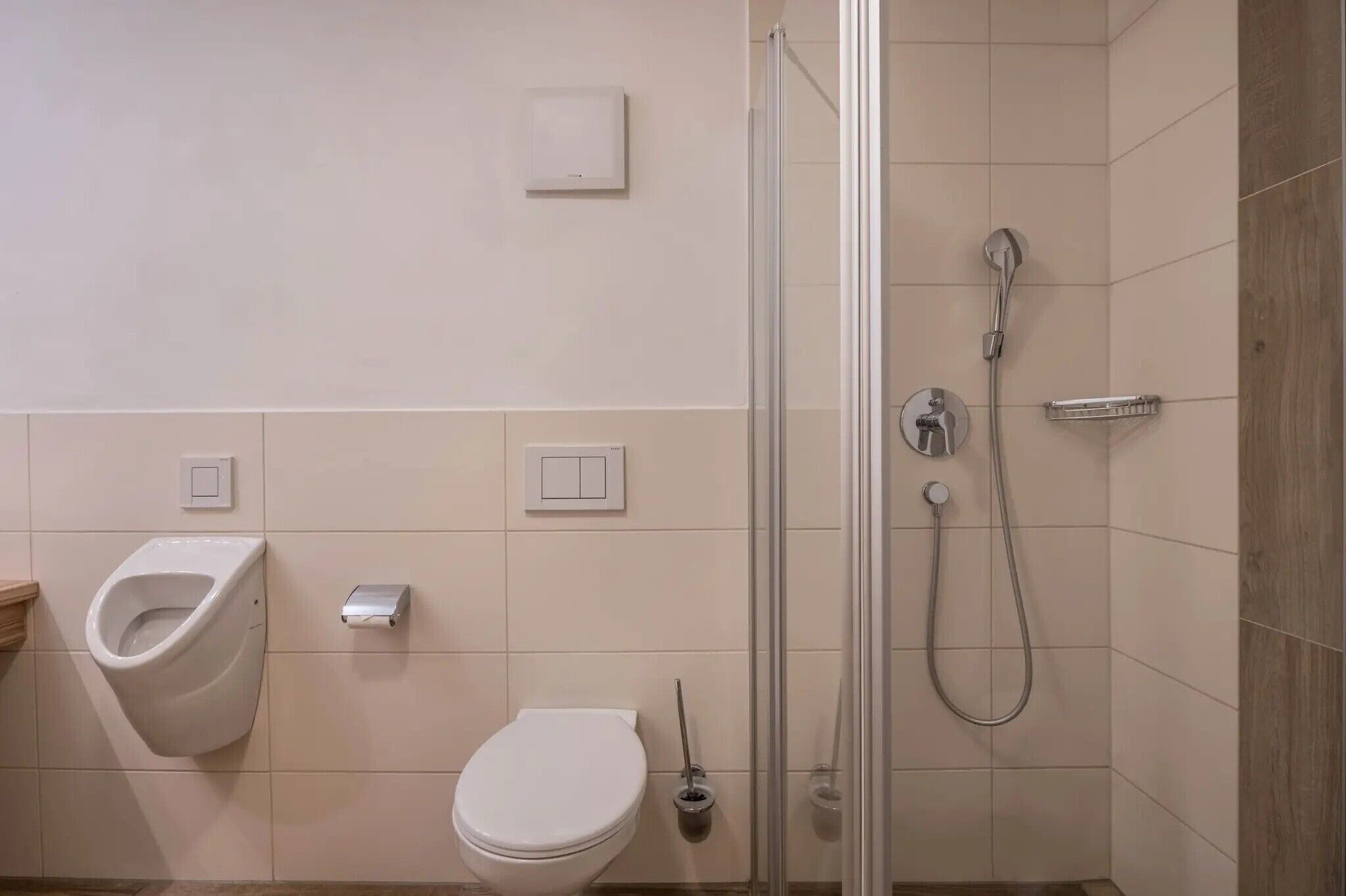 Een moderne badkamer met urinoir, toilet en douchecabine met glazen wanden.