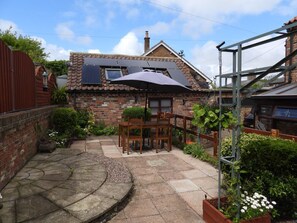 A brick house with solar panels, a patio with a table and chairs, and a garden with various plants. - Eric House: A Cozy Getaway in Muston (Filey)