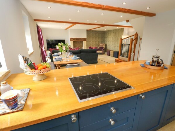 A kitchen with a wooden countertop, a built-in stove, and a dining area in the background. - Black House Cottage, Ripponden (Sowerby Bridge)