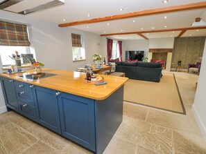 A modern kitchen with blue cabinets, a wooden island, and a dining area with a sofa and TV. - Black House Cottage, Ripponden (Sowerby Bridge)