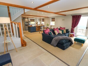 A spacious living area with a sofa set, a staircase, a kitchen, and a view through a window. - Black House Cottage, Ripponden (Sowerby Bridge)