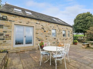 A stone building with a patio, a white table with chairs, and a large window. - Black House Cottage, Ripponden (Sowerby Bridge)