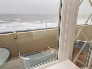 Ein Balkon mit Meerblick, ein Stuhl und ein Glastisch.
