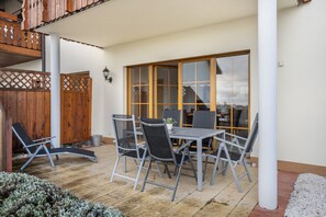 Une terrasse avec une table et des chaises, une clôture en bois et une vue à travers une porte vitrée.