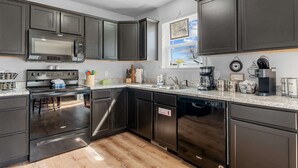 A modern kitchen with dark cabinetry, stainless steel appliances, and a window with a view. - Trolly Inn Hot Tub, Walkable (Branson)