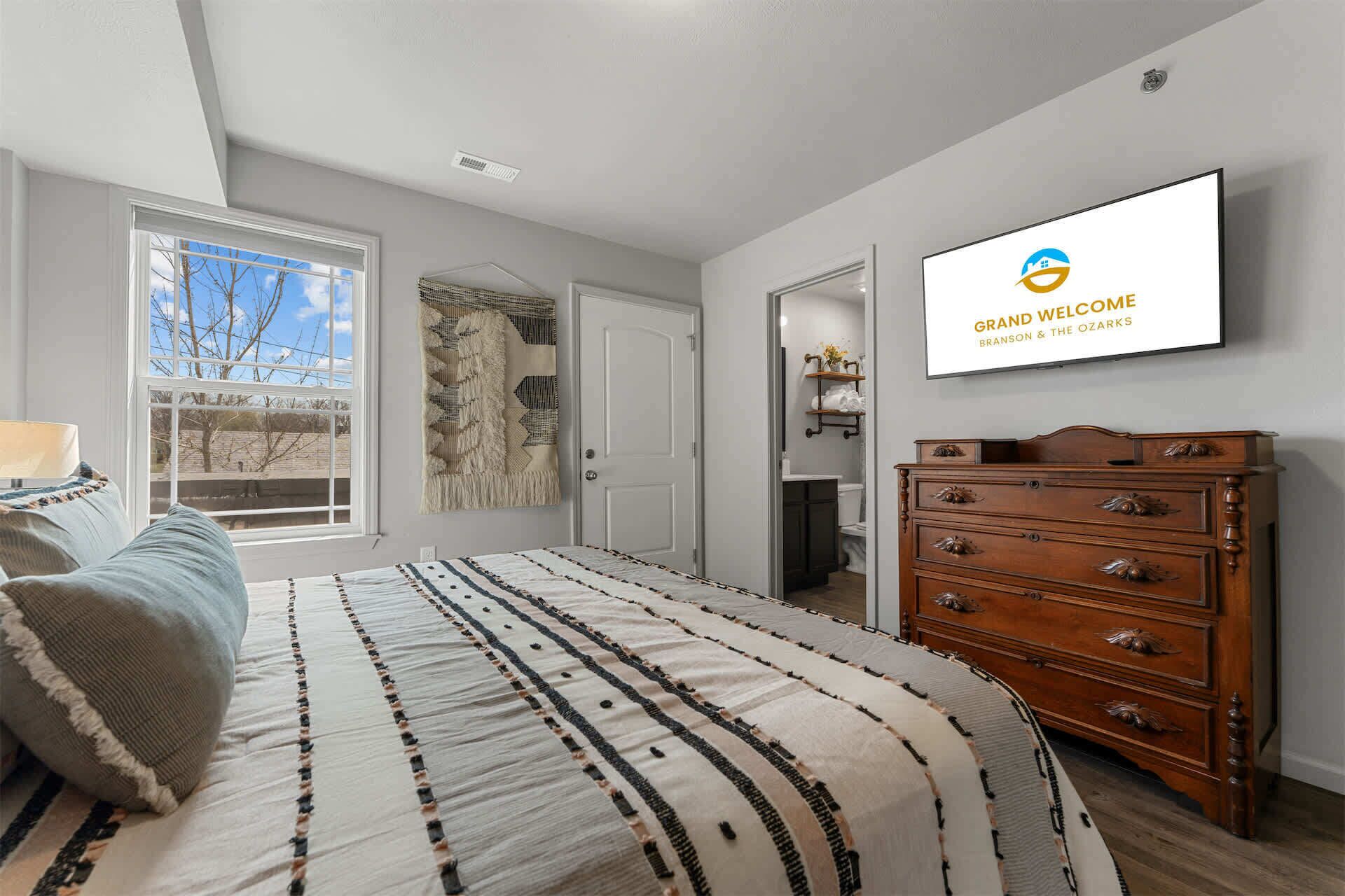 Een slaapkamer met een bed, een dressoir, een wandtelevisie en een raam met uitzicht.