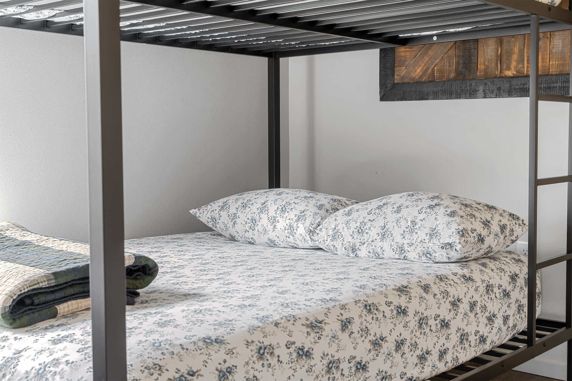Ein Stockbett mit floralem Bettzeug, einem Holz-Kopfteil und einem Metallrahmen.