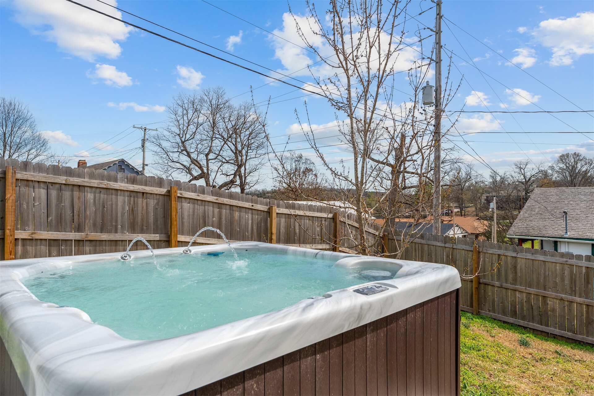 Ein Whirlpool in einem Garten mit Holzzaun, Bäumen und Häusern im Hintergrund.