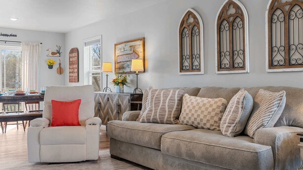 A living room with a striped armchair, a beige sofa with patterned cushions, a dining area with a table and chairs, and decorative wall art. - Trolly Inn Hot Tub, Walkable (Branson)