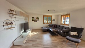 Moderni olohuone, jossa on kulmasohva, televisio ja sohvapöytä.