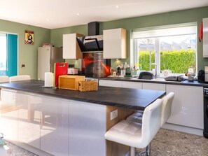 A modern kitchen with a central island, white cabinetry, and a large window providing natural light. - Afallon, Llanerchymedd (Llannerch-y-Medd)