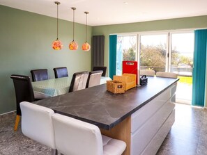 A modern kitchen with a marble countertop, a dining area with chairs, and a large window with curtains. - Afallon, Llanerchymedd (Llannerch-y-Medd)