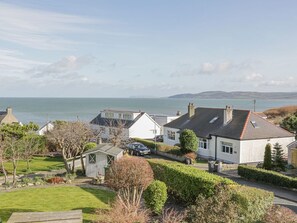 A coastal residential area with houses, a grassy lawn, and a view of the sea. - Seaview in Benllech, Anglesey. (Tyn-y-Gongl)