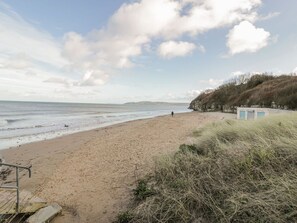 A beach with a sandy shore, a small building, and a grassy hill in the background. - Seaview in Benllech, Anglesey. (Tyn-y-Gongl)