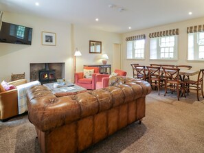 A living room with a fireplace, leather sofa, and dining area with wooden chairs. - Kilnmark Farmhouse in Moniaive (Thornhill)