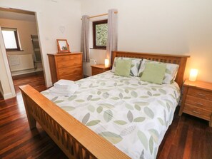 A bedroom with a wooden bed, a nightstand, a dresser, and a window with curtains. - Horse Mill Lodge, Taddington (Buxton)